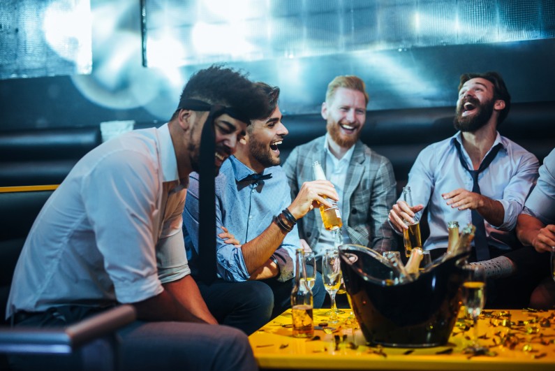 4 men sitting at a bar laughing and drinking